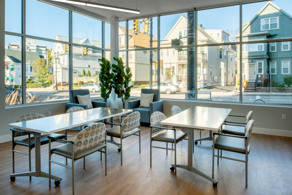 Tables inside of room surrounded by glass windows. Residential multi-families outside.
